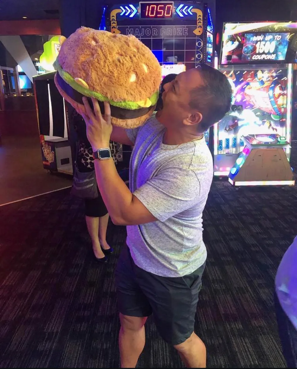 Jeff pretending to bite a giant plush hamburger prize at an arcade